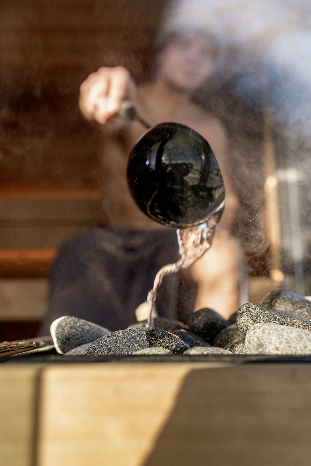 Water poured over hot stones, steam rising in a timber lined room