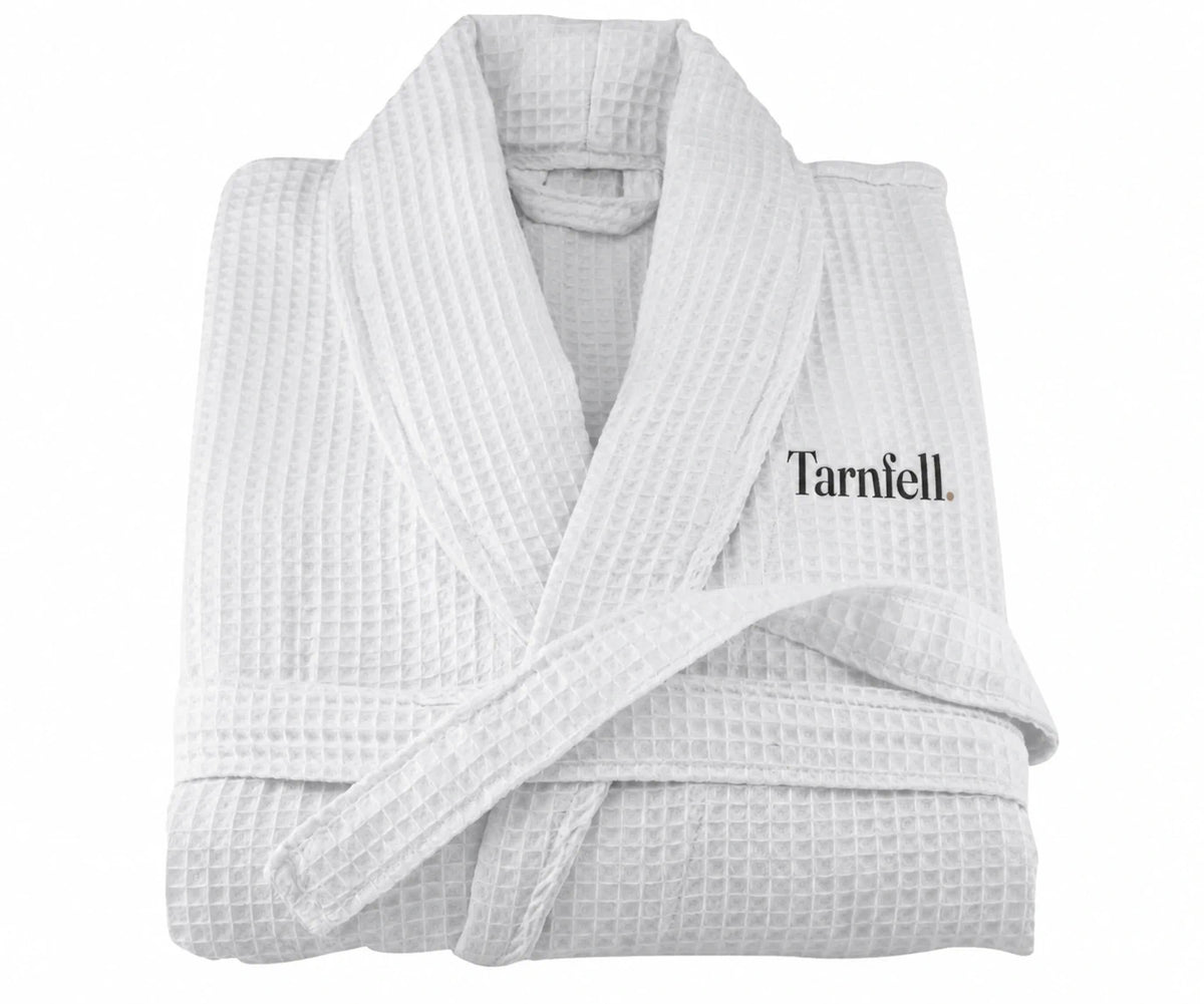 Tarnfell white cotton waffle gown folded, showing the shawl collar, tie belt and the Tarnfell wordmark embroidered on the left chest