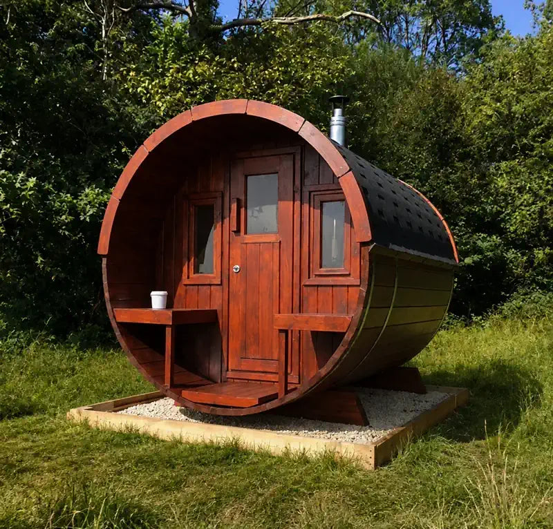 A barrel-shaped 250 wooden sauna cabin with wooden front door, shown outdoors on a grassy lawn with trees in the background.