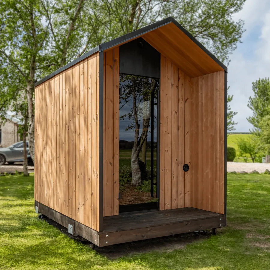 AIRA outdoor sauna installed in a garden, pitched roof and black framed window