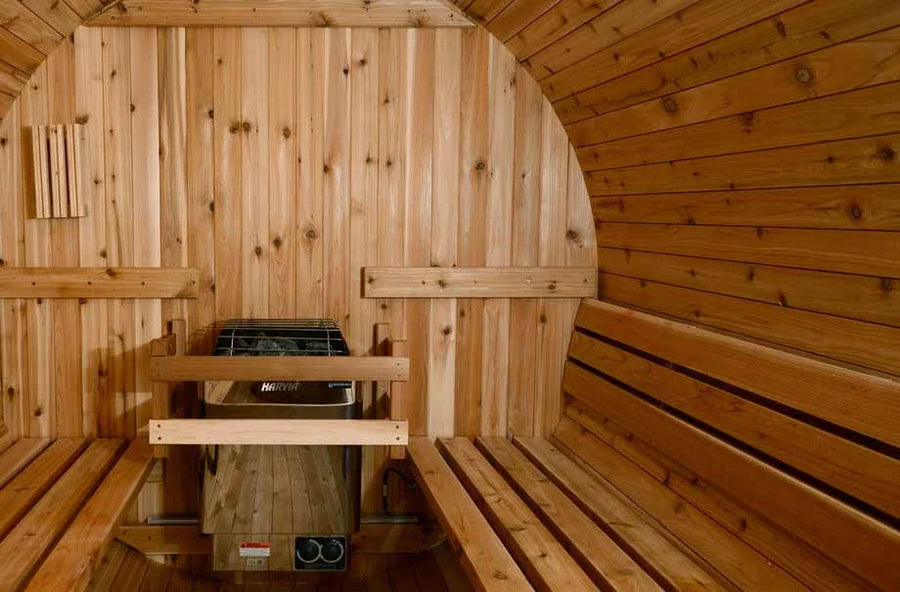 Inside a barrel sauna, two facing benches in cedar with the heater and stones below the bench