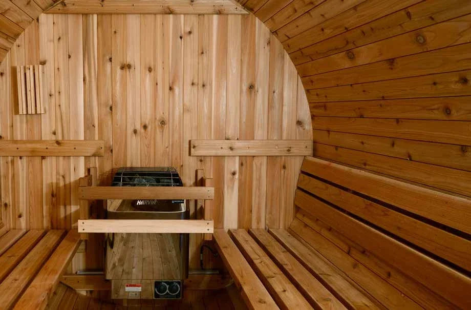 Inside a barrel sauna, two facing benches in cedar with the heater and stones below the bench