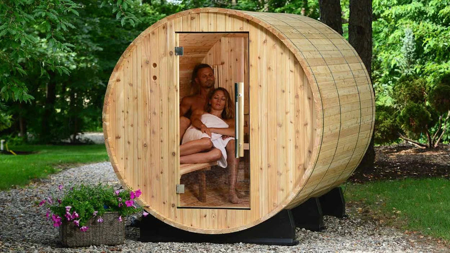 Barrel sauna in a garden with two people seated inside, door open