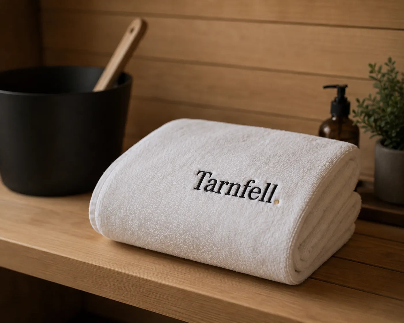 Tarnfell white Microcotton bath sheet folded on a sauna bench, with the Tarnfell wordmark embroidered on the fold